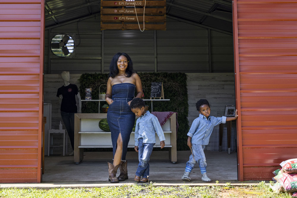 Twin boys standing with their mom in front of a red barn.